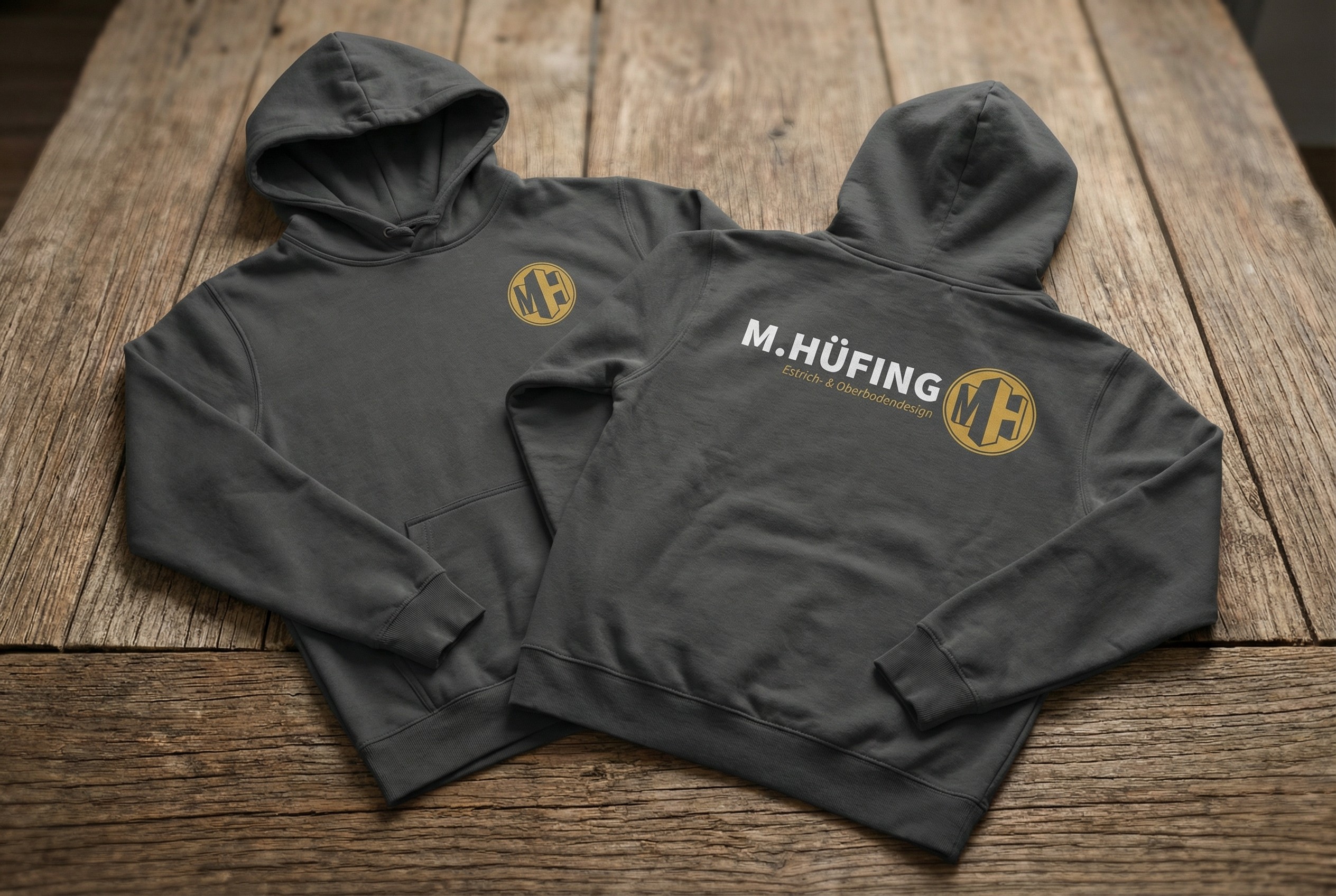 Zwei dunkelgraue Hoodies von M. Hüfing mit Logodruck in Gold und Weiß